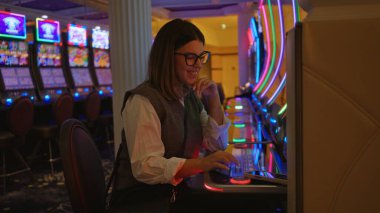 Las Vegas kumarhanesinde oyun oynayan İspanyol bir kadın. Etrafı canlı kumar makineleriyle çevrili. Heyecan ve eğlenceye odaklanmış..