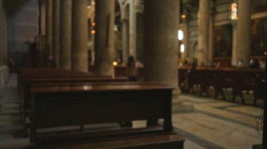 Boş bir kilisenin iç mekânının bulanık görüntüsü banklar ve sütunlarla, kapalı bir yerde, yumuşak bokeh ışıklandırması ve odaklanmış arka plan ile odaksız dini bir ortam sergiliyor..