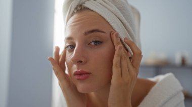 Kaplıca odasında kafasına havlu geçirmiş genç bir kadın. Kapalı mekanda yüzüne dokunuyor. Güzelliğini ve sağlığını gösteriyor.