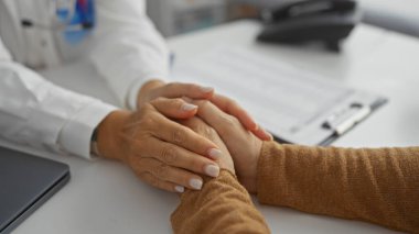 Doktorlar klinikteki hastaları el ele tutuşarak rahatlatıyor, profesyonel bir sağlık hizmetinde şefkat ve bakımı ön plana çıkarıyor, kapalı mekanlarda konuşmalar yapan iki kadını da içeriyor.