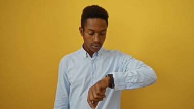 İzole edilmiş sarı arka plana bakan genç Afrikalı Amerikalı adam zaman farkındalığı gösteriyor.