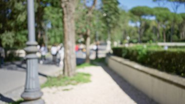 Villa borghese bahçelerinde, Roma 'da ağaçların ve yeşilliklerin arasında yürüyen insanların bulanık görüntüsü, dağılmış figürler ve doğa ile huzurlu bir açık hava ortamı vurguluyor..