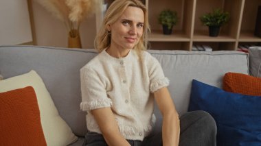 Şık bir oturma odasında, rahat bir kanepede uzanan bir kadın, güzel sarı saçlarını ve sıcak gülümsemesini, modern dekorlar ve yumuşak yastıklarla sarmalanmış..