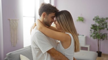 Erkekler rahat bir oturma odasında kadınları kucaklıyor, aşk, ilişki ve mutluluk sergiliyor, modern bir ev ortamında doğal ışık ve basit dekorlarla..