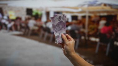 Endonezya rupia banknotlarını kalabalık bir açık hava kahve dükkanının önünde, şehir merkezinde bir iş anlaşmasını temsil ediyor..
