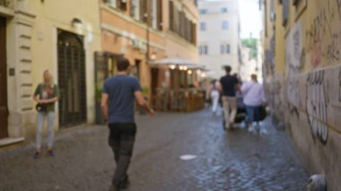 Bulanık insanlar Roma 'da tarihi bir caddede gezerken açık hava kafeleri ve eski mimariyle şehir yaşamını ve atmosferini gün ışığında yakalıyorlar..