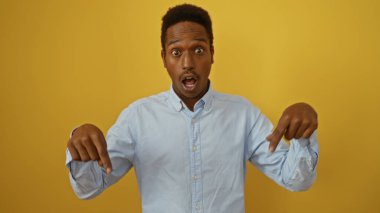 Açık mavi gömlekli genç Afro-Amerikan bir adam, parlak sarı bir arka plana karşı şaşırmış görünüyor.