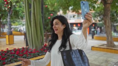 Şehir parkında gülümseyen kadınlar, kentin arka planında ağaçlar ve çiçeklerle çevrili dostluk ve neşe gösteren selfie çekiyorlar.