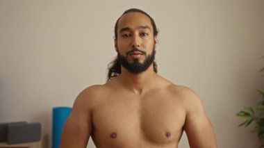 Sakallı genç adam spa salonunda gülümsüyor. Rahatlama ve sükunet sergiliyor. Kapalı mekanda minimalist bir dekor ve huzurlu bir ortam sunuyor..