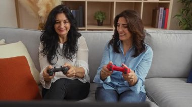 Kanepede video oyunları oynayan, orta yaşlı kadınları sergileyen, mutlu ve rahat bir atmosferi olan rahat bir oturma odasında birlikte eğlenen kadınlar..