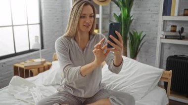 Akıllı telefondan gülümseyen ve konuşan bir kadın. Yatak odasında, rahat bir yatak odasında, doğal ışık ve kapalı mekan bitkileriyle..