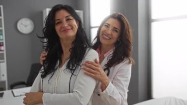 Mutlu kadınlar, doktor ve hasta, yakın çevresindeki tıbbi ekipmanlarla aydınlık, modern bir klinikte birlikte gülümsüyorlar, güven ve özeni vurguluyorlar..