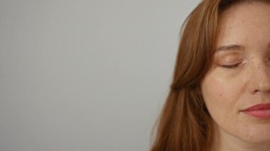 Beyaz arka planda kızıl saçlı bir kadın, sakin ve izole bir ortamda doğal bir güzellik yayar. Çekici özelliklerini ve Kafkas kökenini ön plana çıkarır..