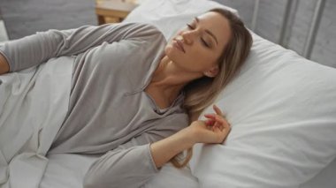 Akıllı telefon kullanan, rahat bir şekilde yumuşak yastıklarda uzanan, rahat atmosferli, sarışın, yetişkin, sabah haberlerinden keyif alan, günlük kıyafetlerini giyen bir kadın..