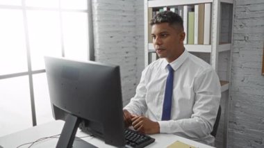 Beyaz gömlekli ve mavi kravatlı bir bilgisayar kullanarak ofiste çalışıp başarıyı kutlayan İspanyol bir adam.