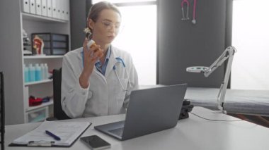 Steteskoplu kadın doktor, klinikteki bir video konsültasyonu sırasında, masadaki bir dizüstü bilgisayarla, teletıp ve sağlık hizmetleri iletişimini vurgulayan haplar tutuyor..
