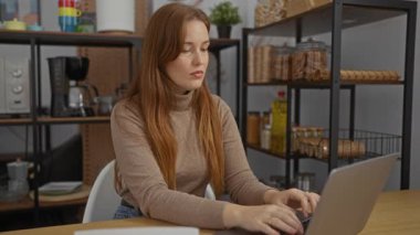 Evde dizüstü bilgisayarla çalışan bir kadın, ofis ortamındaki belgelere bakıyor, kızıl saçlı, yetişkin, çekici, profesyonel görünümlü..