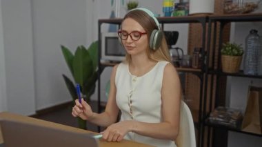 Kulaklıklı bir kadın, ofis ortamındaki bagetler gibi kalemleri vururken odaklanmış görünüyor. Etrafı bitki ve raflarla çevrili. Rahat bir çalışma alanı titreşimi veriyor..