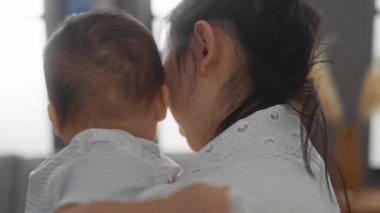 Aile evde dinleniyor, anne kucağında bebek ve baba rahat bir oturma odasında dizüstü bilgisayar kullanıyor..