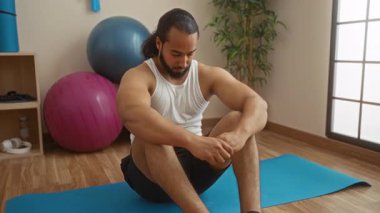 Spor topları ve bitkilerle sağlık odasında yoga minderinde oturan bir adam, bir fitness stüdyosunda tefekkür ve gevşemeyi ifade ediyor..