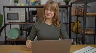 Görevdeki genç kadın, modern iç unsurlar ve raflardaki dekorlarla çevrili dizüstü bilgisayarla olumlu bir çalışma ortamı ve profesyonel atmosferi gösteriyor..