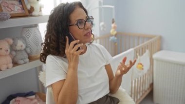 Yatak odasında beşikle konuşan bir kadın, oyuncaklarla çevrili, ev ortamında olgun bir dişinin olduğu bir ev içi görüntü sergiliyor..