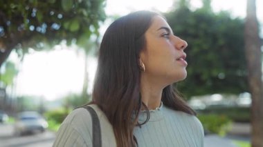 Kadın şehir parkında geziyor, kumral saçlı, açık şehir çevresiyle çevrili, şık giyinmiş, sakin bir şehir hayatı hissi uyandırıyor..