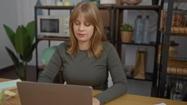 Parlak ofis çalışma alanındaki bir kadın telefona şaşırmış gibi görünüyor. Beklenmedik bir şekilde hareketli içeriği karşısında şaşkınlık ifadesi sergiliyor. Masanın üzerinde iç mekan bitkileri ve ofis malzemeleri var..