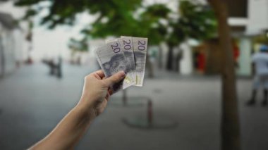 Şehir arka planında ve ağaçlarda bulanık bir şehir caddesinde el ele tutuşan İsviçre banknotları, açık hava para transferlerinin özünü yakalıyor..