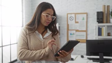 Modern ofis ortamında çalışan kadınlar, ofis malzemeleri ve doğal aydınlatmalarla çevrili özgüvenli ve odaklanmış bir tablet kullanıyorlar, üretkenliği ve teknolojiyi benimsiyorlar..