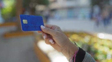 Elinde mavi bir kredi kartı olan şehir geçmişi bulanık elini ve şık bileziğini gösteren bir kadın..