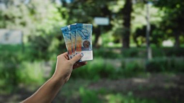 Parkta İsviçre frangı tutan bir adam. Arkaplan gibi canlı bir yeşillik, açık hava para değişimi sahnesini yakalıyor..