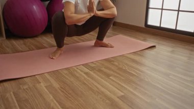 Orta yaşlı bir kadın spor salonundaki paspasın üstünde yoga yapıyor. İç mekanda spor toplarıyla denge ve sağlığa odaklanıyor..