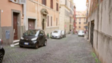 Roma, İtalya 'da parke taşından yapılmış klasik arabaların ve tarihi mimarinin olduğu bulanık bir sokak manzarası. Eski dünya cazibesiyle bulanık bir şehir atmosferi yaratıyor..