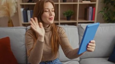 Kitaplar ve bitkilerle çevrili, rahat oturma odasında, rahat bir ev atmosferini doğal ışık ve sıcak renklerle gösteren tablet kullanan bir kadın..