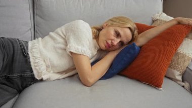 Oturma odasındaki rahat bir kanepede dinlenen, beyaz bir kazak giyen, evde rahat bir sabah rutini gösteren bir kadın..