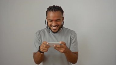 Örgülü genç adam beyaz arka planda hareketli bir oyundan zevk alıyor. Mutluluk, konsantrasyon ve merak gibi duygular gösteriyor. Günlük kıyafetler giyiyor..