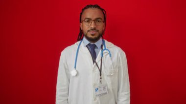 Beyaz önlüklü, parlak kırmızı arka planda steteskoplu, kendine güvenen gülümseyen doktor, profesyonelliği ve yakınlığı somutlaştıran genç siyahi adam.