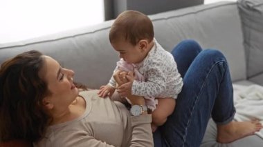 Oturma odasındaki kanepede bebekle oynayan bir kadın aile sevgisini ve yakınlığını gösteriyor..