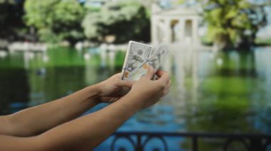 Parkta Amerikan dolarlarını tutan bir adam açık hava zenginliği kavramını vurgulayan yemyeşil bir çevreye sahip..