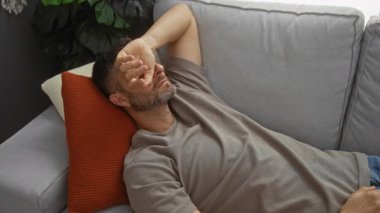 Rahat bir evde kolları bağlı bir kanepede dinlenen genç bir adam, rahatlama ve kapalı bir yaşam tarzını ön plana çıkarıyor..