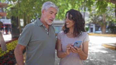 Güneşli bir şehir parkında selfie çeken orta yaşlı bir çift sıcak bir günde aşk, mutluluk ve kadın arasında bir bağ sergiliyor..