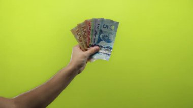 Parlak sarı bir arka plana karşı Kanada dolarları tutan adam, tecrit edilmiş bir ortamda finansal bolluk ve zenginliği vurguluyor..