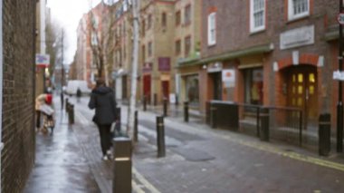Londra 'daki şehir caddesi, arka planda tarihi binalar bulunan yedi kadranda kış boyunca ıslak kaldırımlarda yürüyen bulanık yayaları gösteriyor..