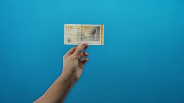 Danimarka kronu banknotunu izole edilmiş mavi bir arka plan üzerinde tutan adam Danimarka 'dan gelen parayı basit ama çarpıcı bir kompozisyonda gösteriyor..