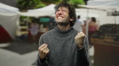 Kalabalık bir şehir caddesinde, arka planda çadırların altında insanların kaynaşmasını kutlayan genç bir adam.