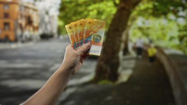 Bir şehir caddesinde İsviçre banknotları tutan adam, canlı bir şehir ortamında döviz ve finans kavramlarını sergiliyor..