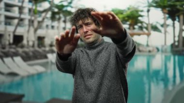 Genç adam, açık havada havuzun önünde el hareketleriyle jesti durduruyor..