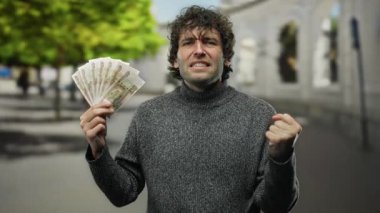 Bir şehir caddesinde elinde Rus rublesi banknotları tutan İspanyol bir adam para ve kentsel çevre üzerine yoğunlaşarak çeşitli duygular ifade ediyor..