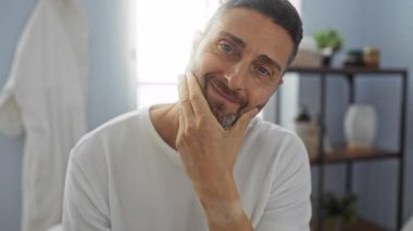 Sakalı sakin bir spa ortamında tımar eden bir adam, sakin bir iç atmosferi olan, kendine özen göstermeyi vurgulayan, sağlıklı bir odada genç ve çekici bir İspanyol erkeği ön plana çıkarıyor..